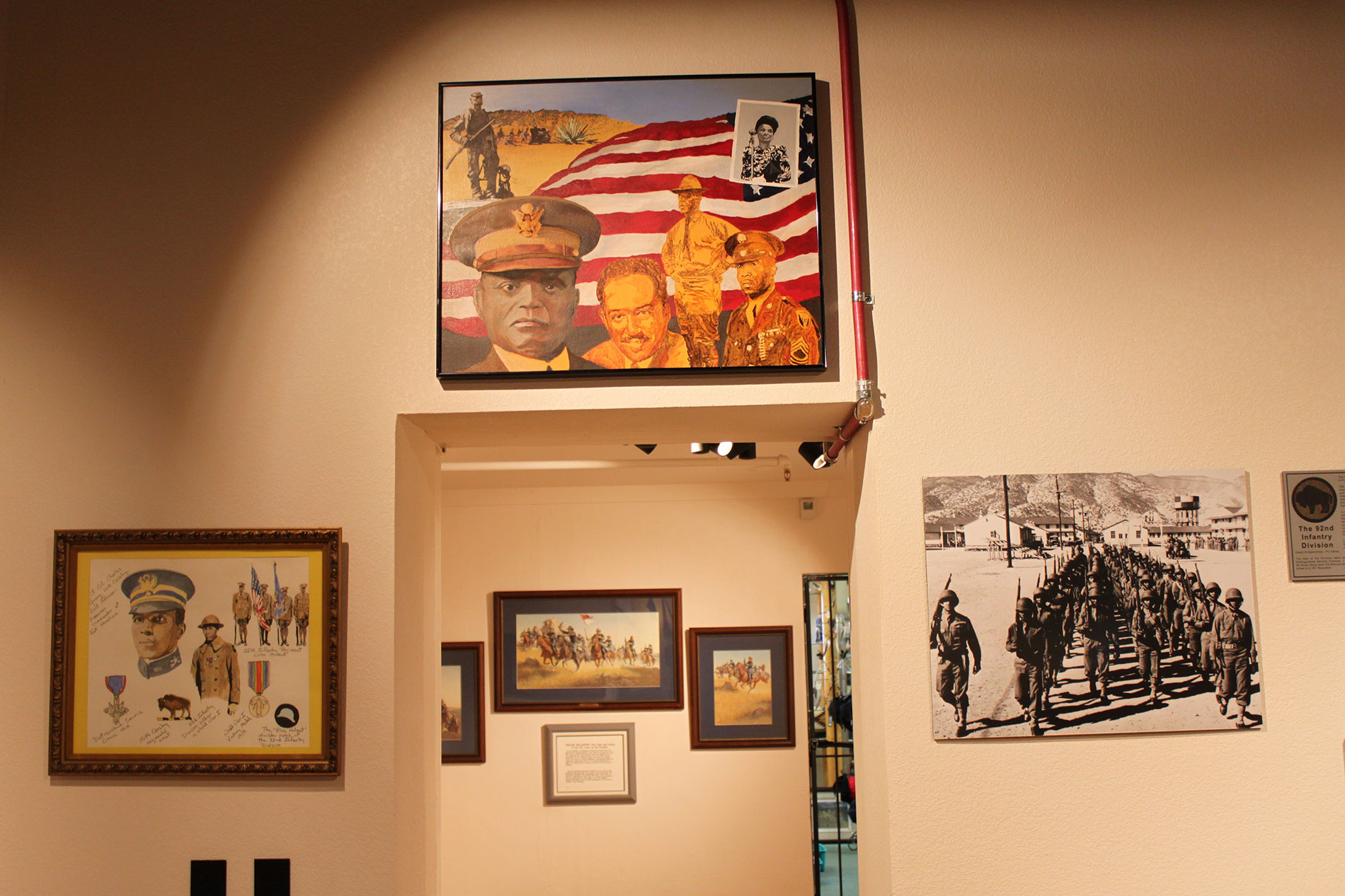 Several framed pictures hanging on a wall and over a doorway inside a museum.